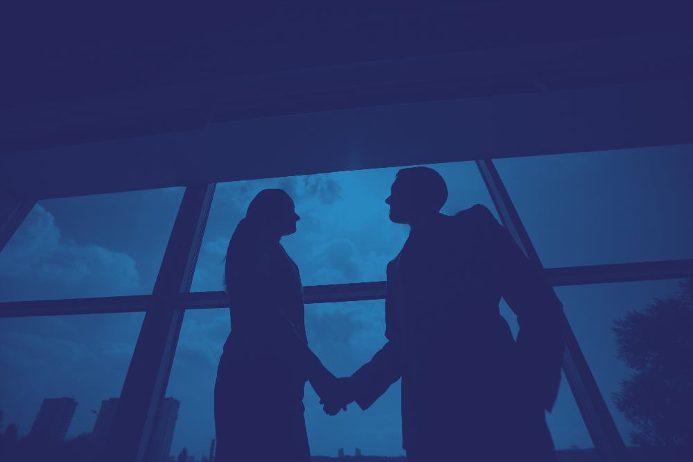 Stretta di mano tra due professionisti davanti a una vetrata